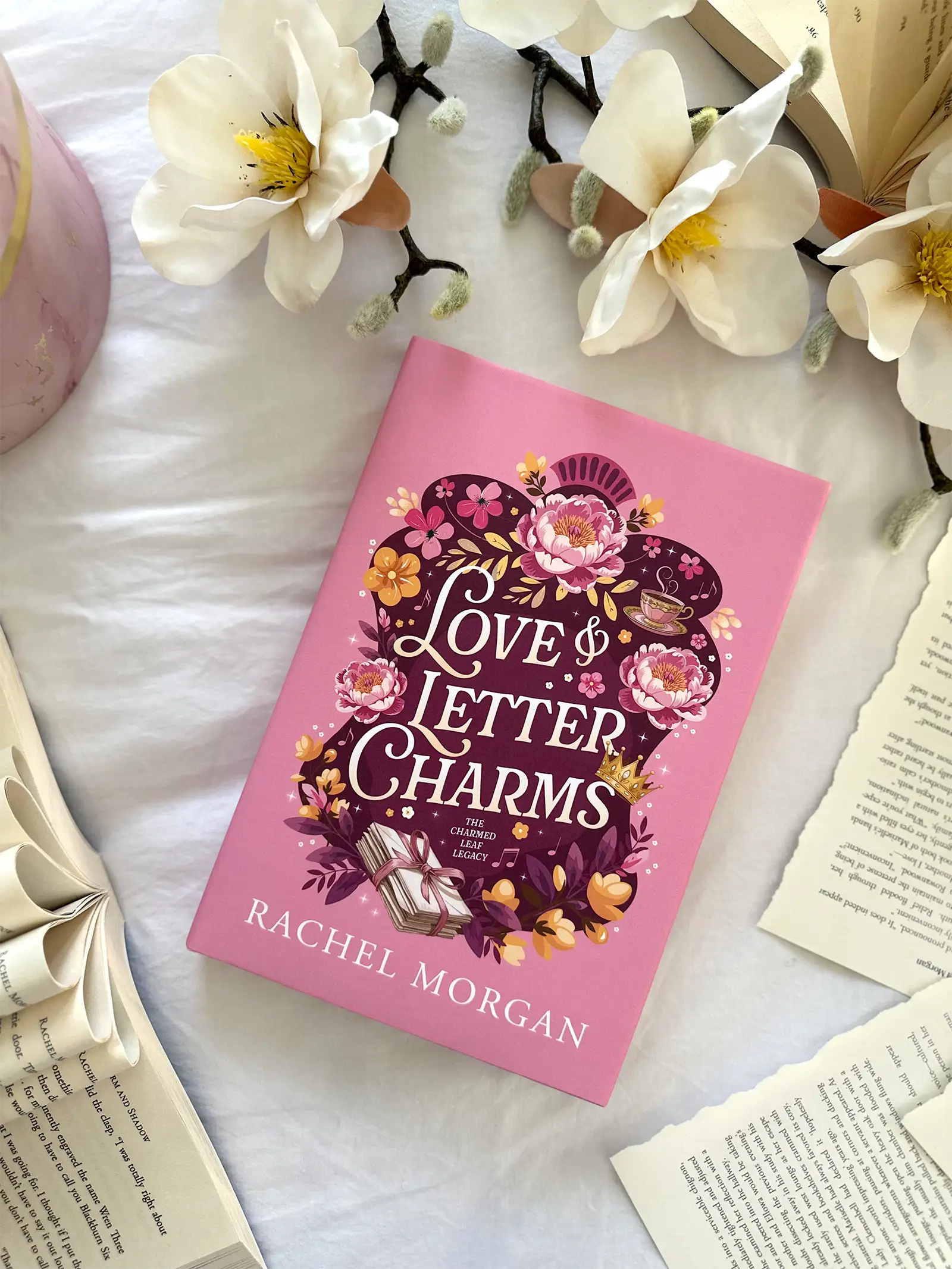 A flat lay of the Love & Letter Charms special edition hardback, styled with flowers and loose book pages.