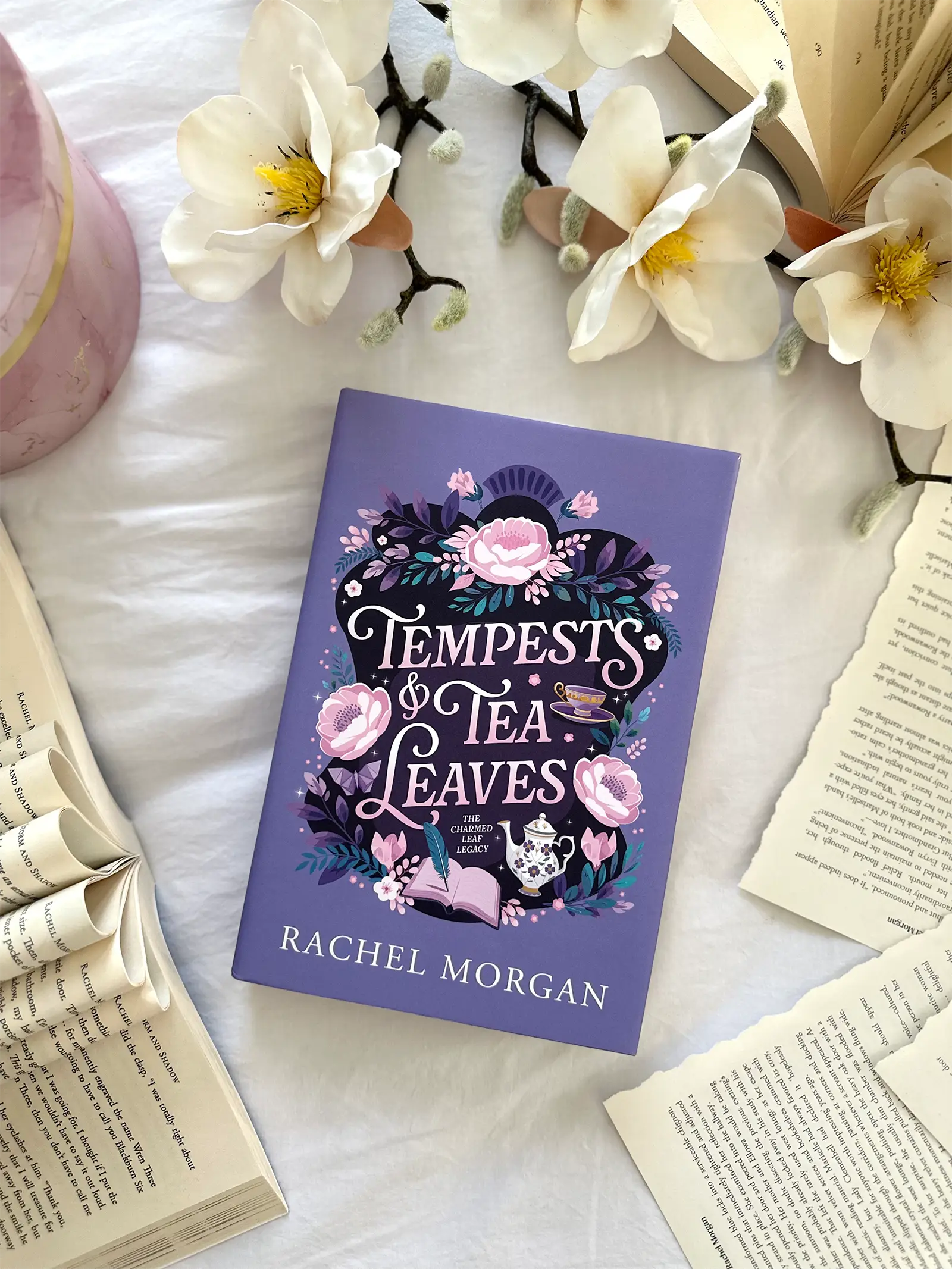 A flat lay of the Tempests & Tea Leaves special edition hardback, styled with flowers and loose book pages.